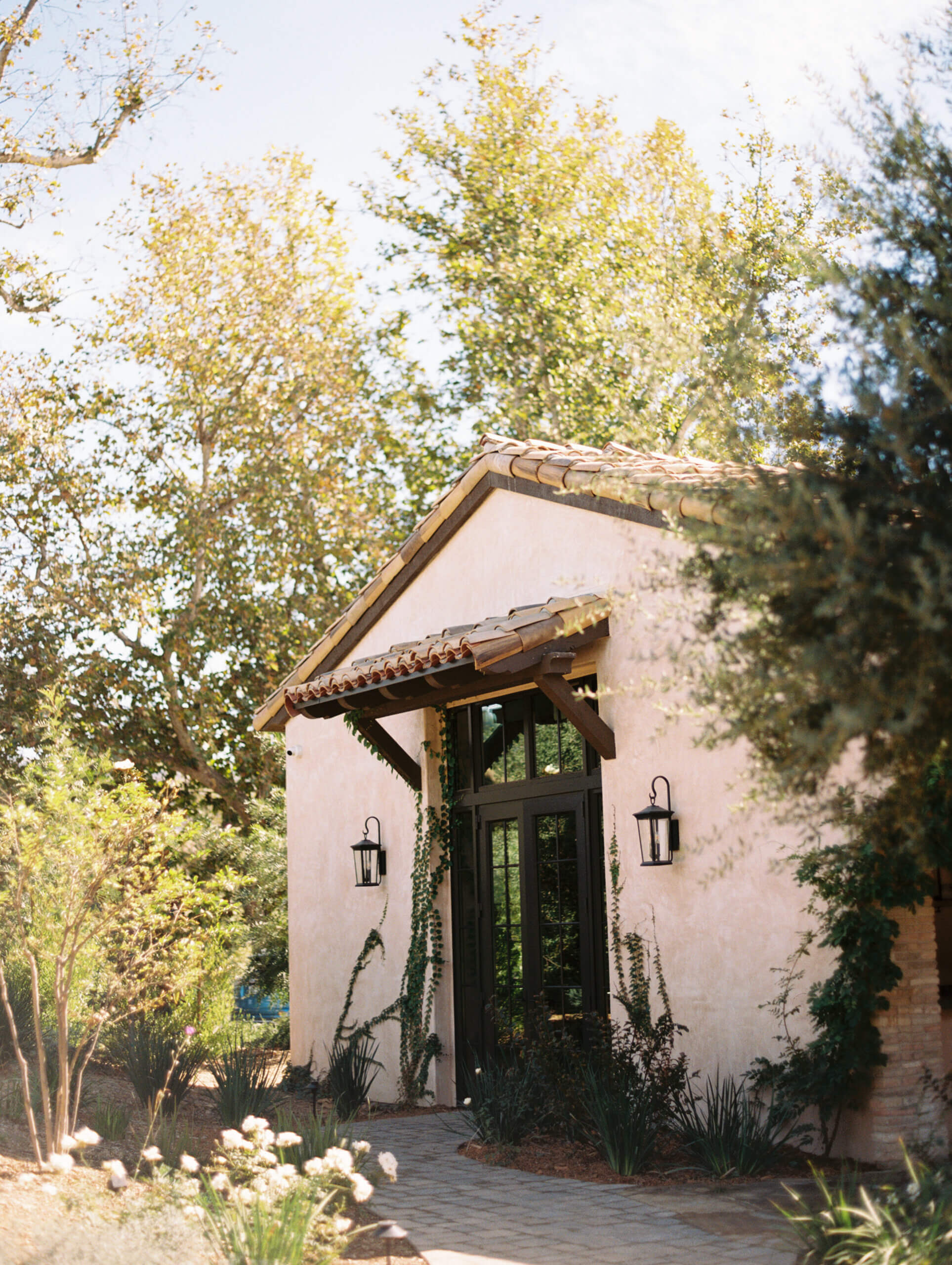the grooms prep space at monserate winery, a beautiful building with tile roof, and modern industrial glass and black doors surrounded by a ton of plants
