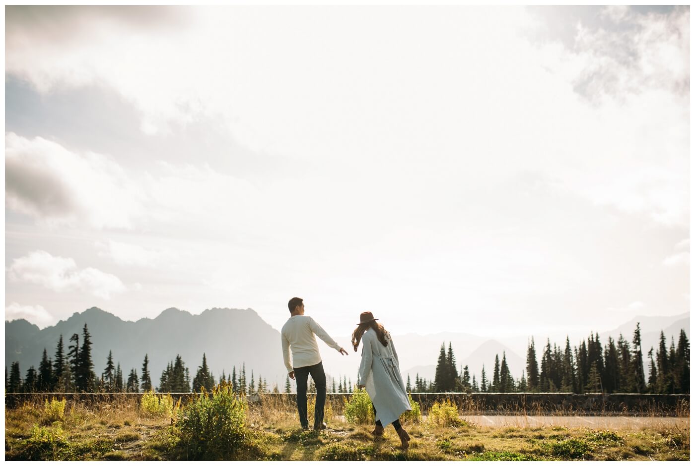 mt rainier engagement session - a bride and groom walking together with a scenic view for their engagement photographer
